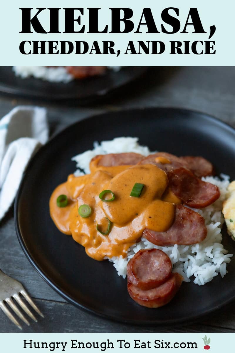 Rice and sausage with cheese sauce on a black plate.