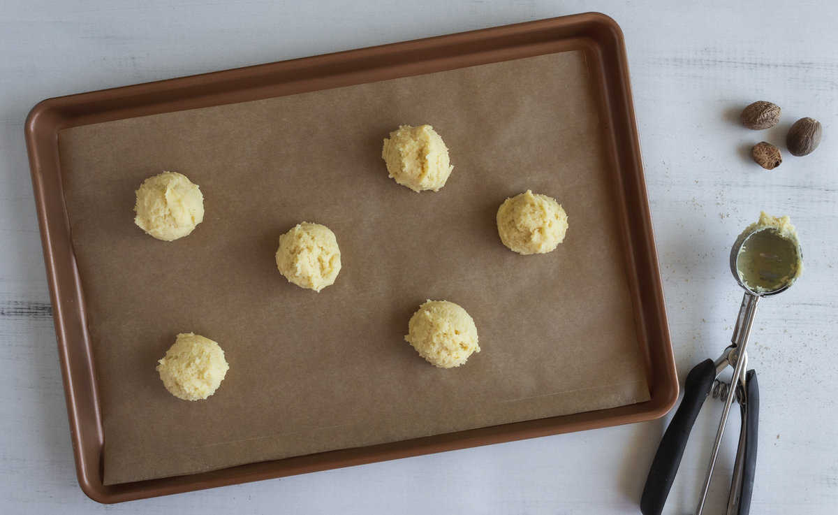 Scoops of white cookie dough on a lined baking sheet.
