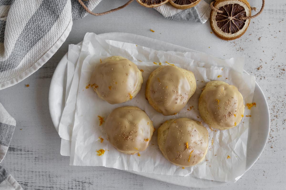 Iced cookies on sheets of paper and with grated nutmeg and orange zest over tops.