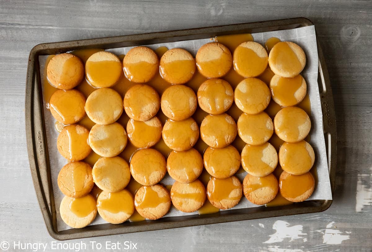 Rows of cookies on a sheet pan with toffee sauce poured over.