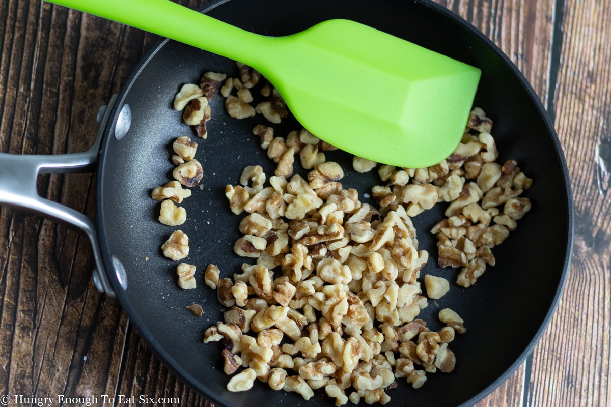 Walnuts in a small skillet with a green spatula