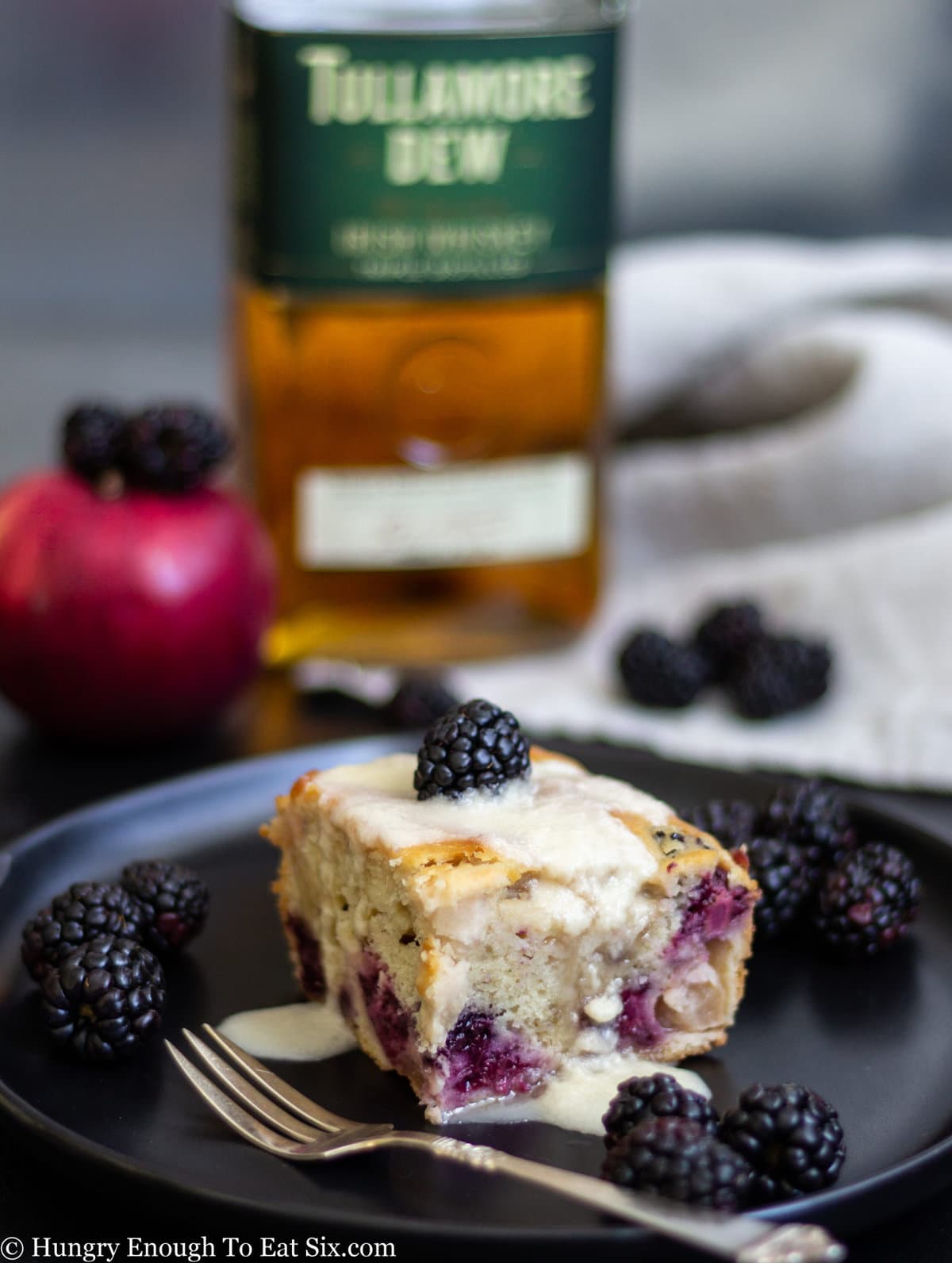 Berry filled cake slice on a plate with a bottle of whiskey in the background