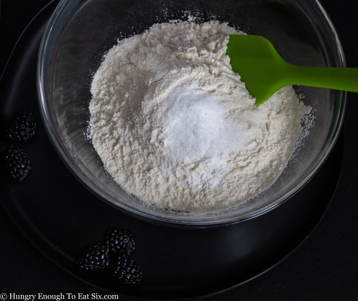 Flour and dry ingredients in a glass bowl with a green spatula
