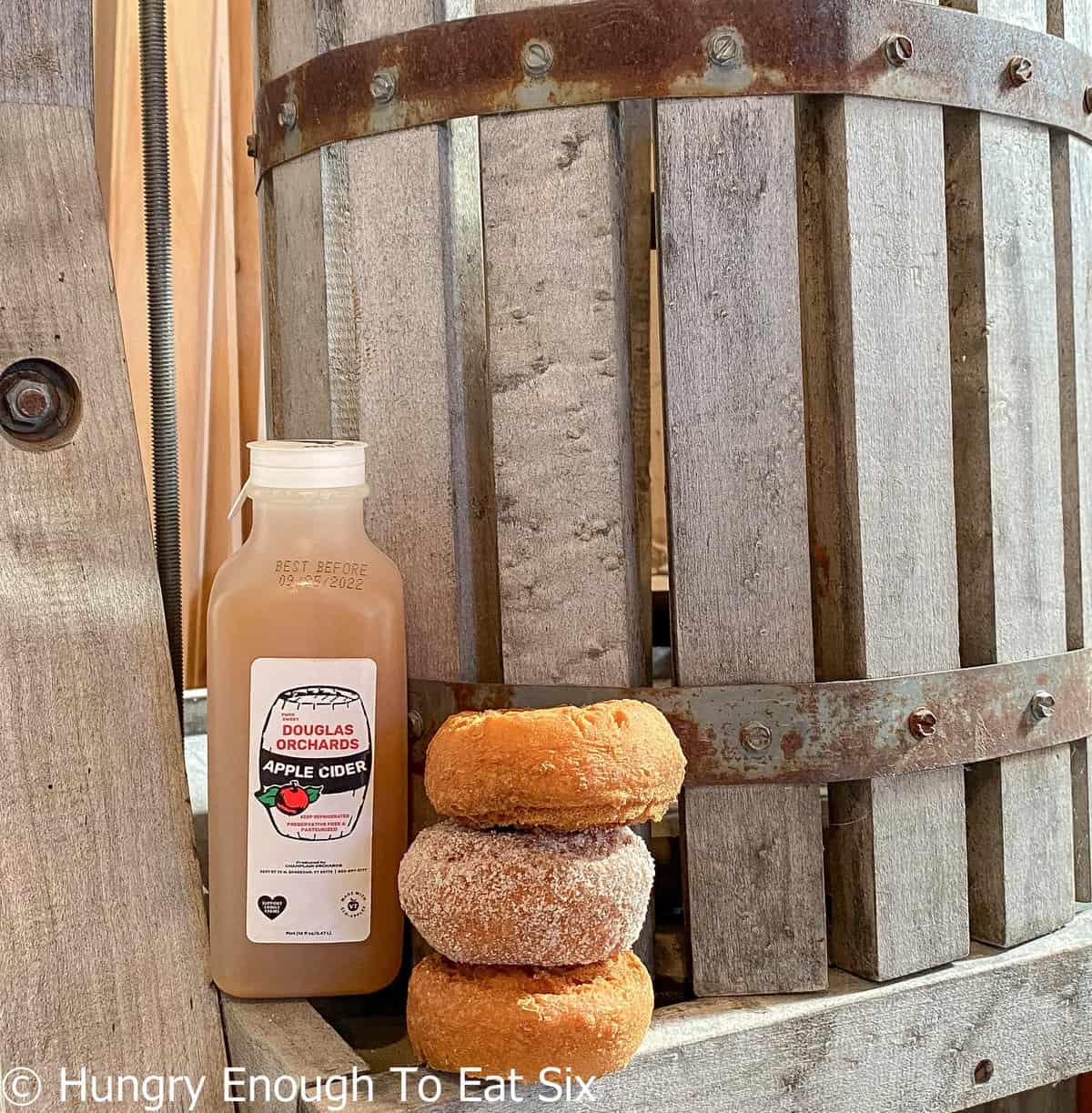 Donuts and bottle of cider next to wooden apple press.