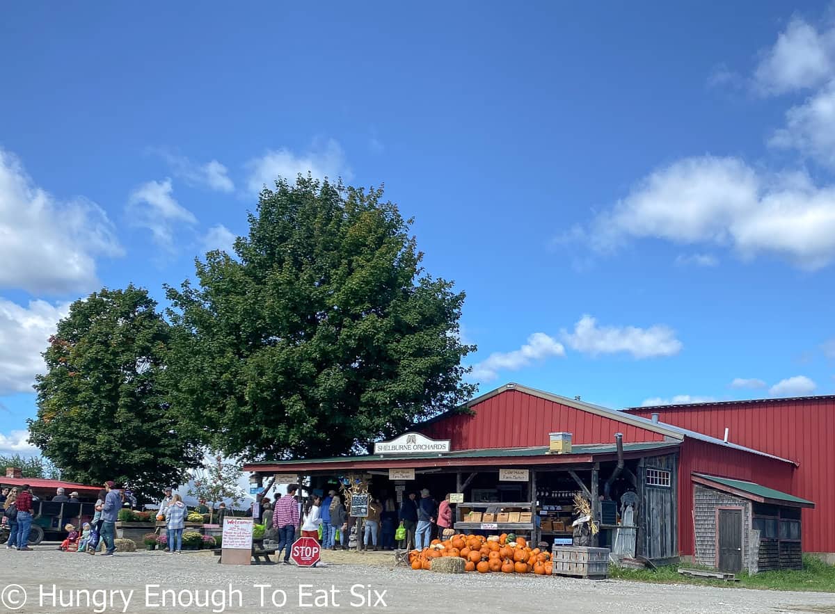 Red barn and farm stand with people and pumpkins. 