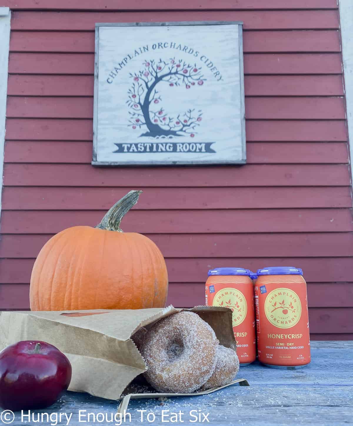 Donuts, cider, and pumpkins against red barn siding. 
