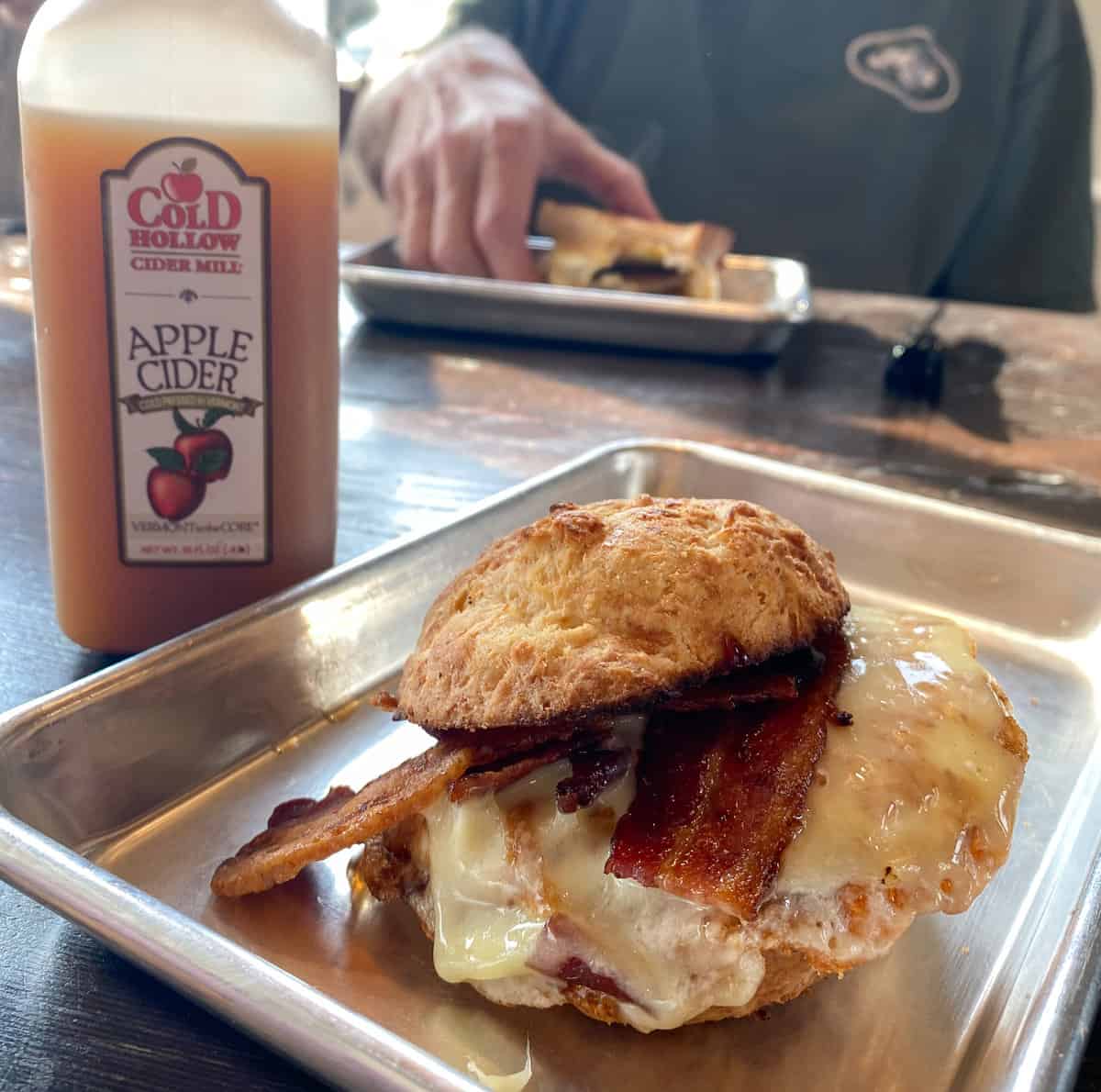 Bacon egg breakfast sandwich on tray with bottle of cider.