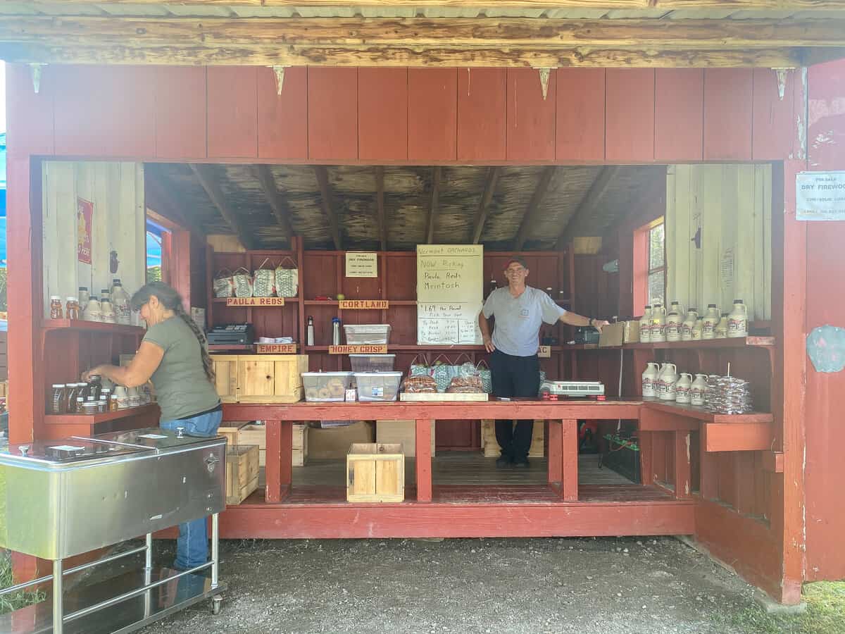 Farmstand with red walls and counter and man in hat standing behind counter.