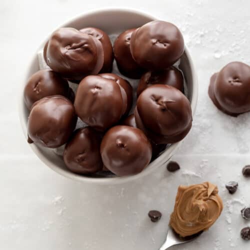 Shiny chocolate covered peanut butter balls in a white bowl.