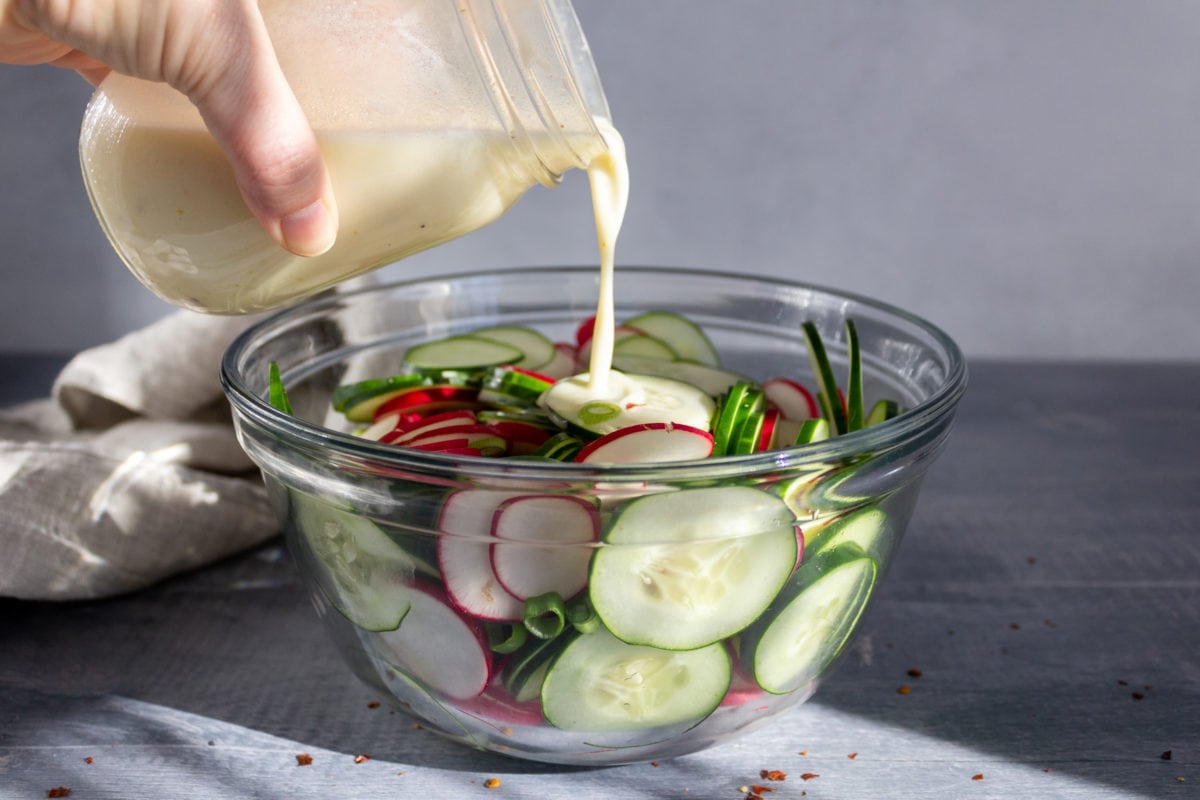 Bowl of sliced vegetables with dressing pouring in