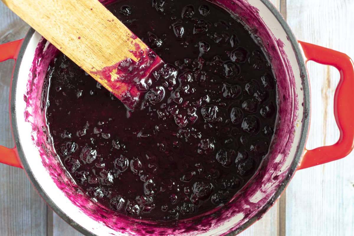 Enameled pot full of reddish purple blueberry sauce.