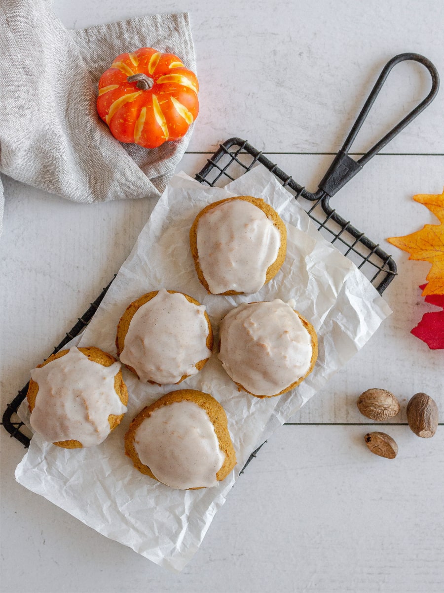Five frosted pumpkin cookies on a wire rack.