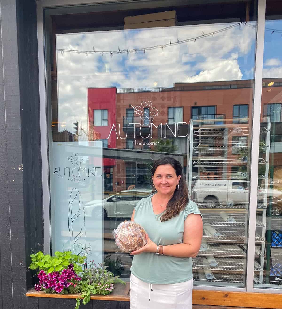 Woman holding loaf of bread outside bakery window.
