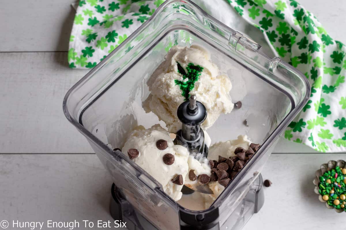 Ice cream, chocolate chips, and green food coloring inside a blender.