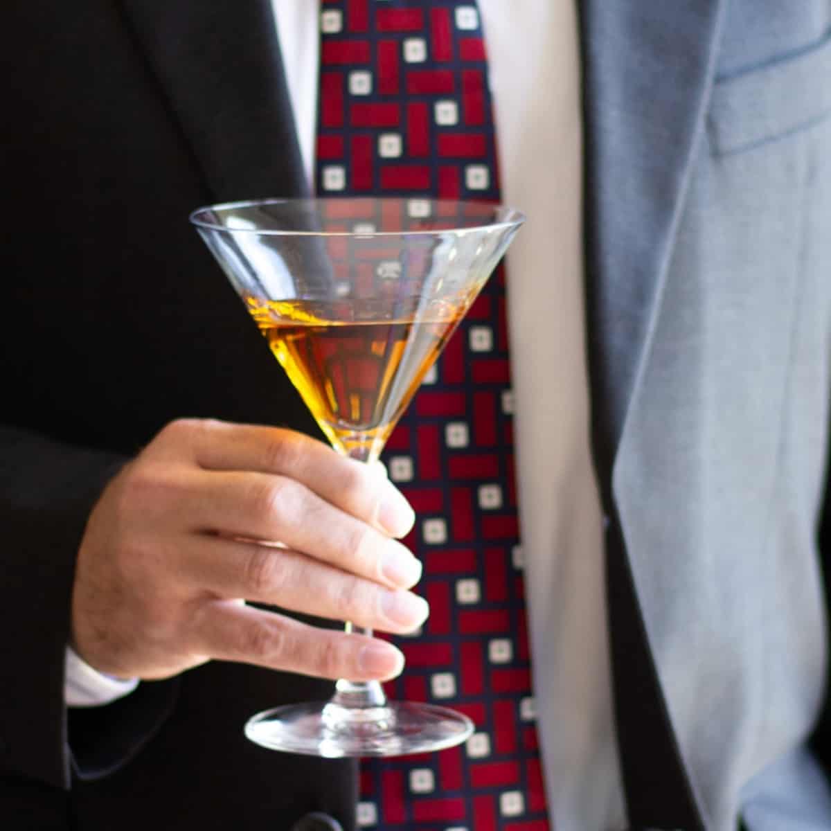 Hand holding golden-colored cocktail in glass.