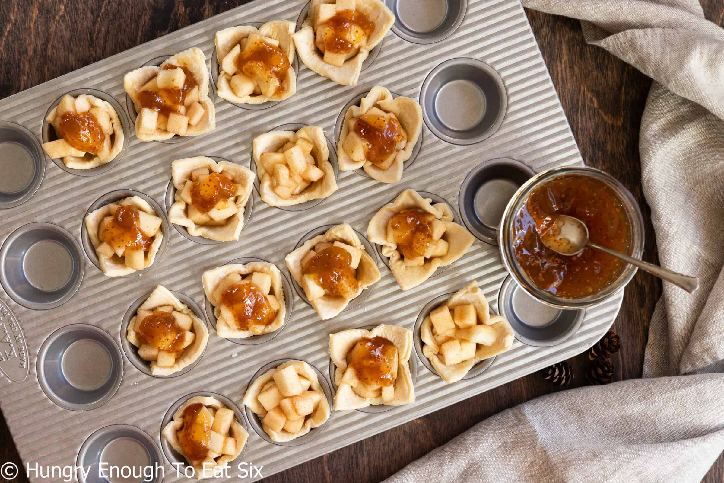 Raw puff pastry shells holding diced apple, brie, and fig.