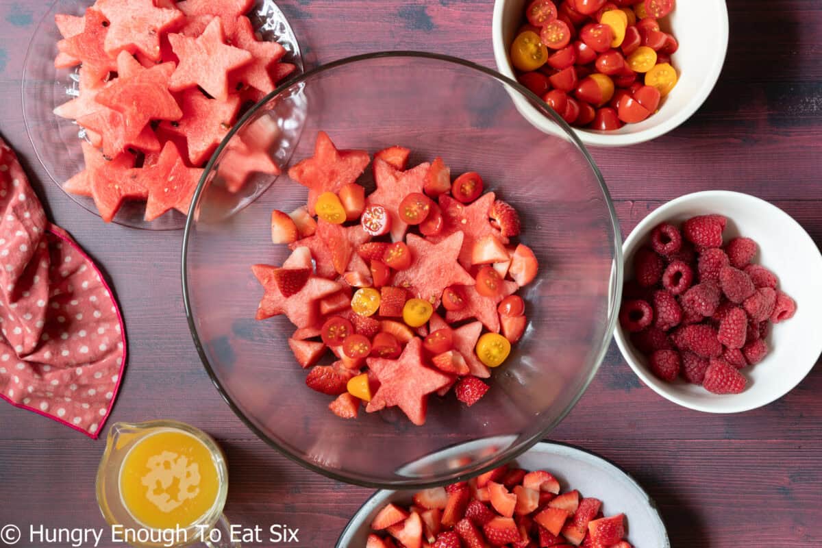 Glass bowl with red fruits and sliced cherry tomatoes.