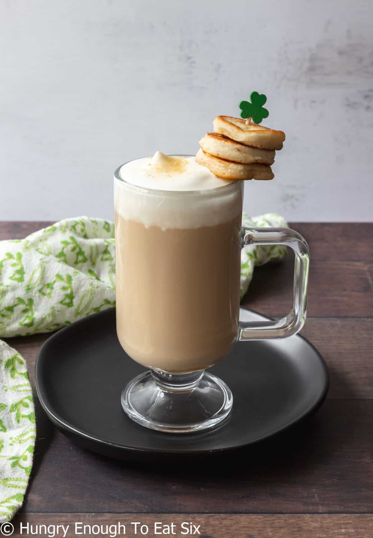 Glass of Irish coffee with cream top and pancakes garnish.
