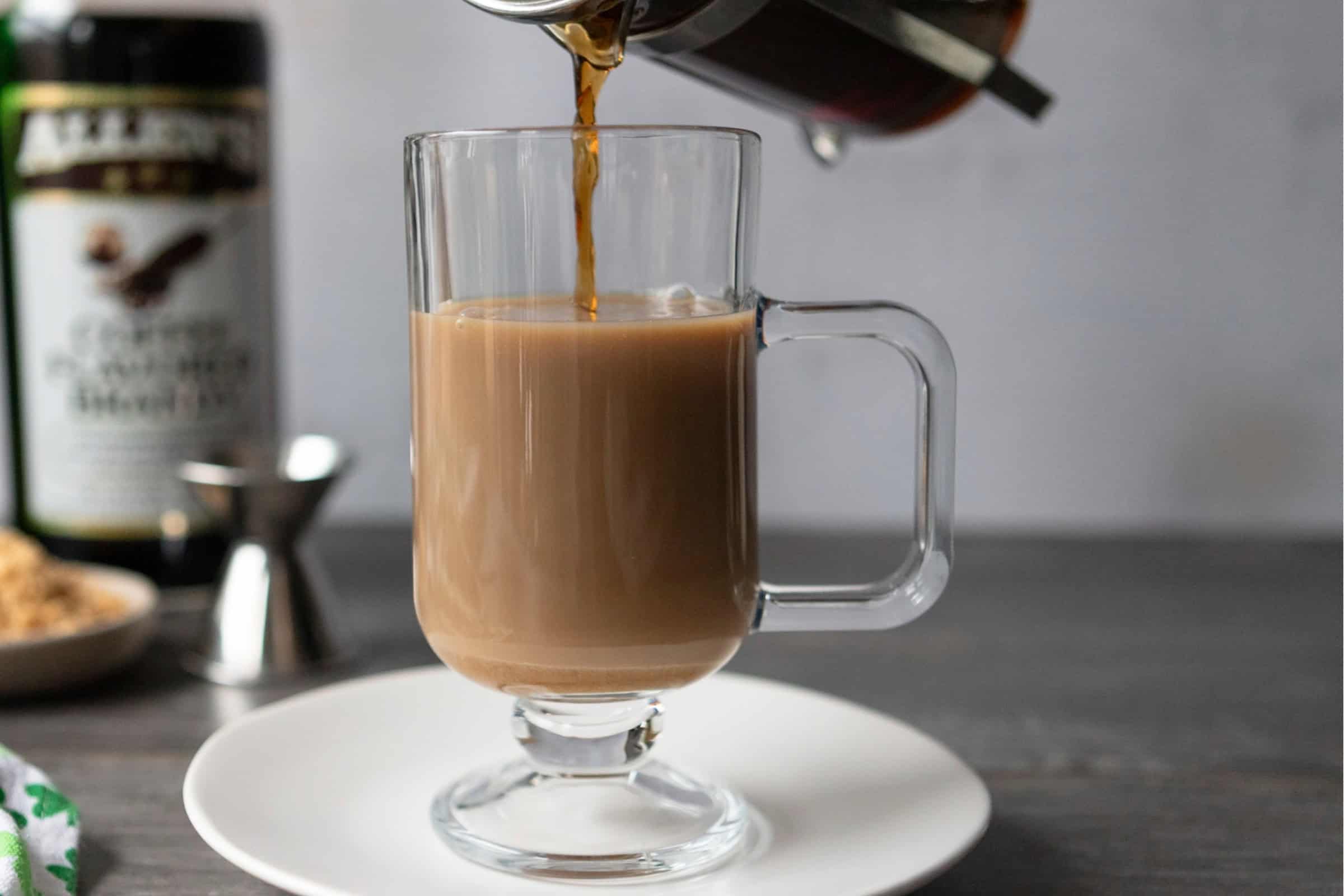 Pouring coffee into a glass with Irish whiskey and brandy, for a coffee brandy Irish coffee.