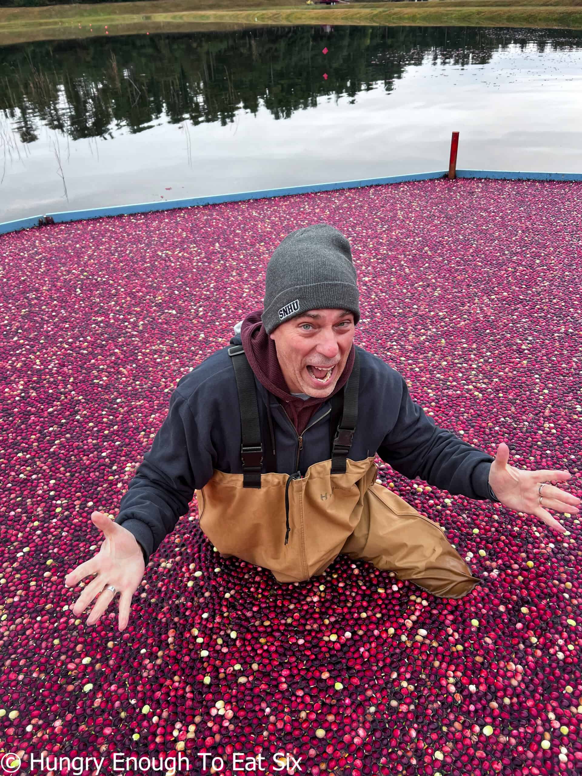 Man standing in water surrounded by cranberries.