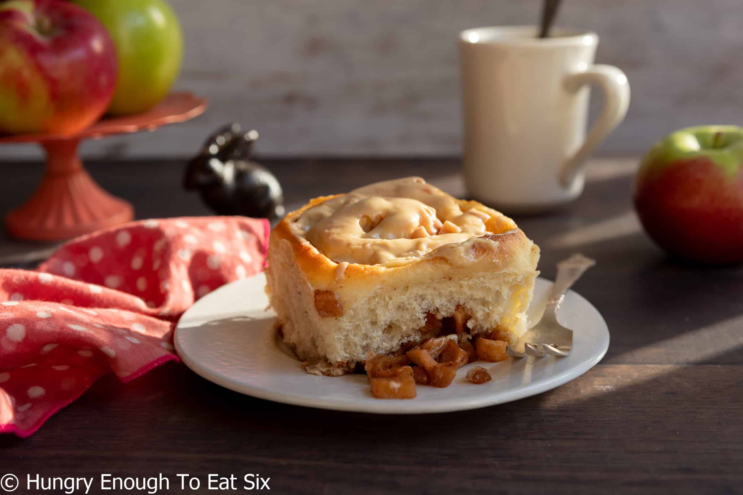 Cinnamon roll on a plate with coffee behind.