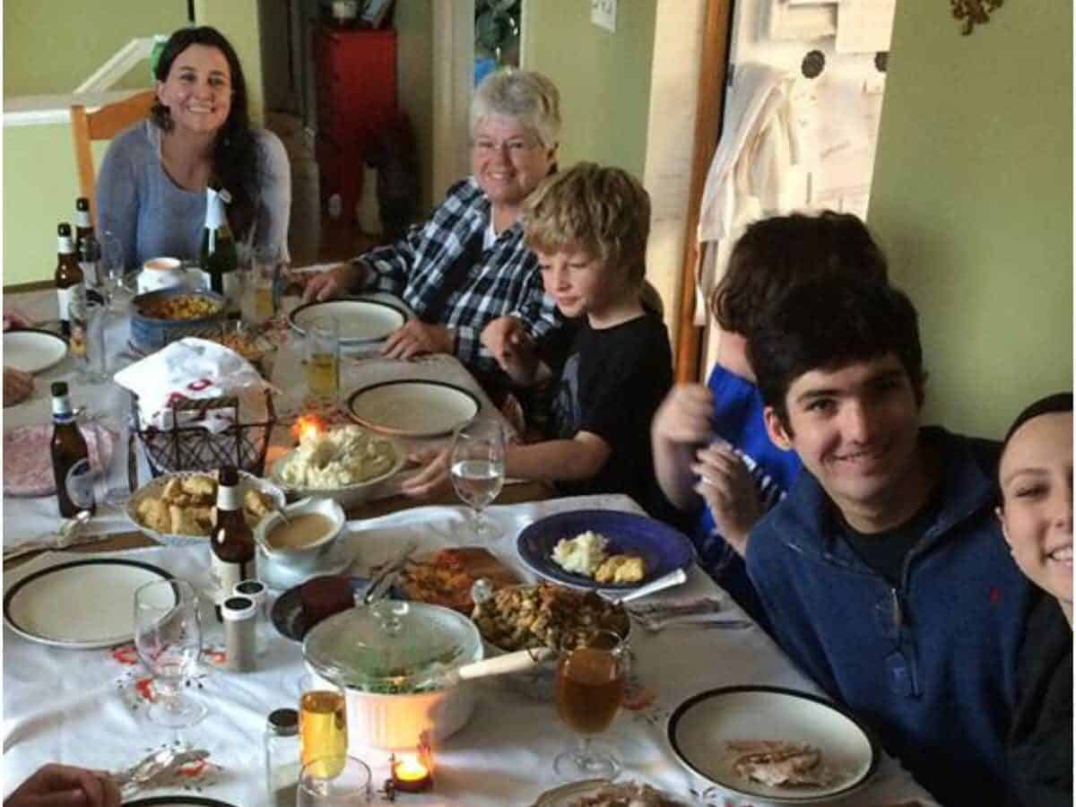 Long table with Thanksgiving food on platters and people seated close together for the meal.
