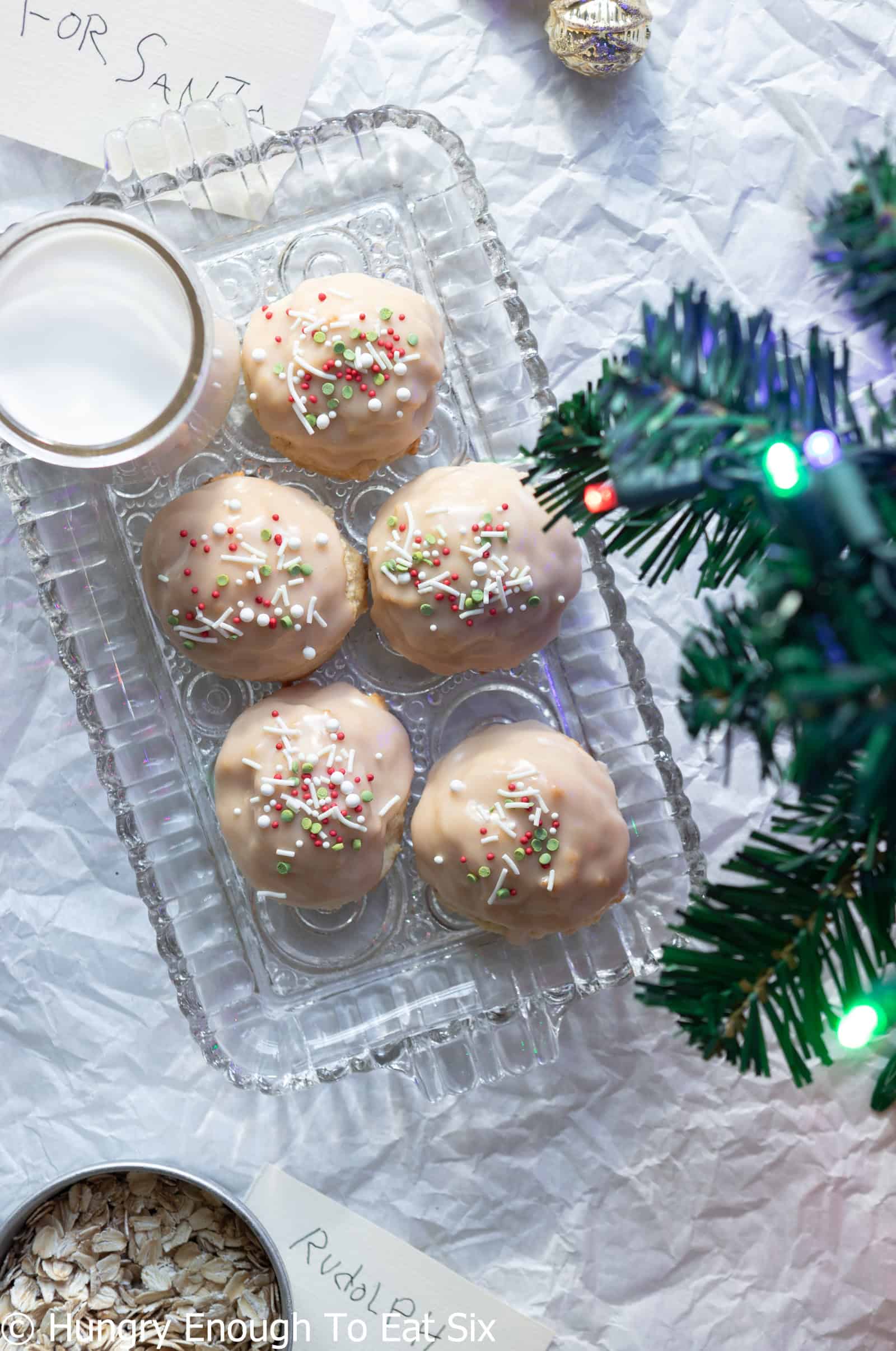 Glass plate with decorated Iced Vanilla Cozy-Ups soft sugar cookies near a glass of milk.