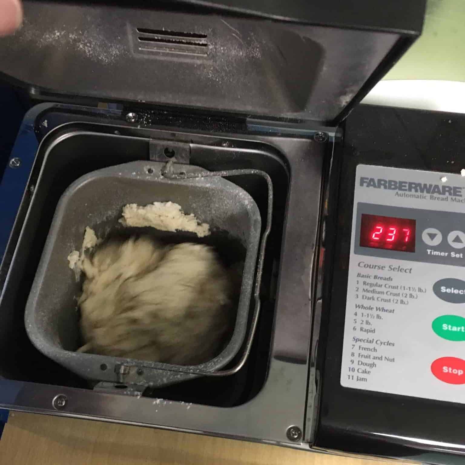 Bread machine on a table with dough mixing inside.