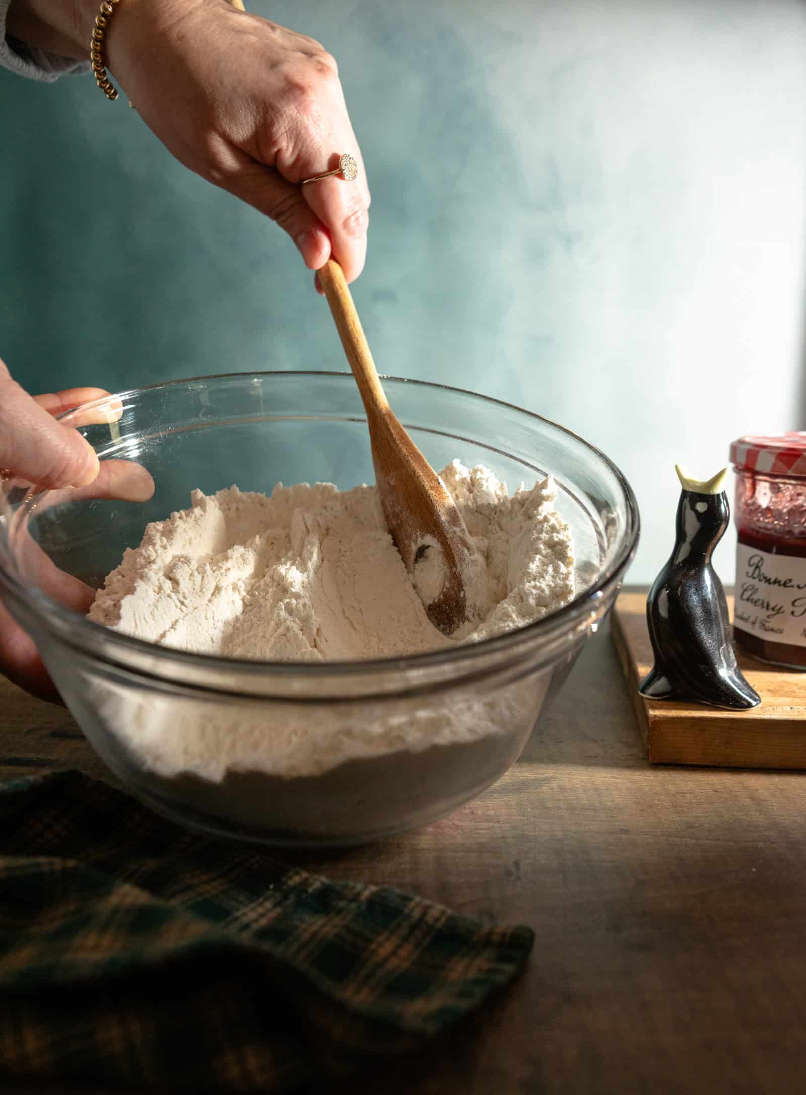 Glass bowl with dry ingredients for buttermilk spoon, and a hand stirring with a spoon.