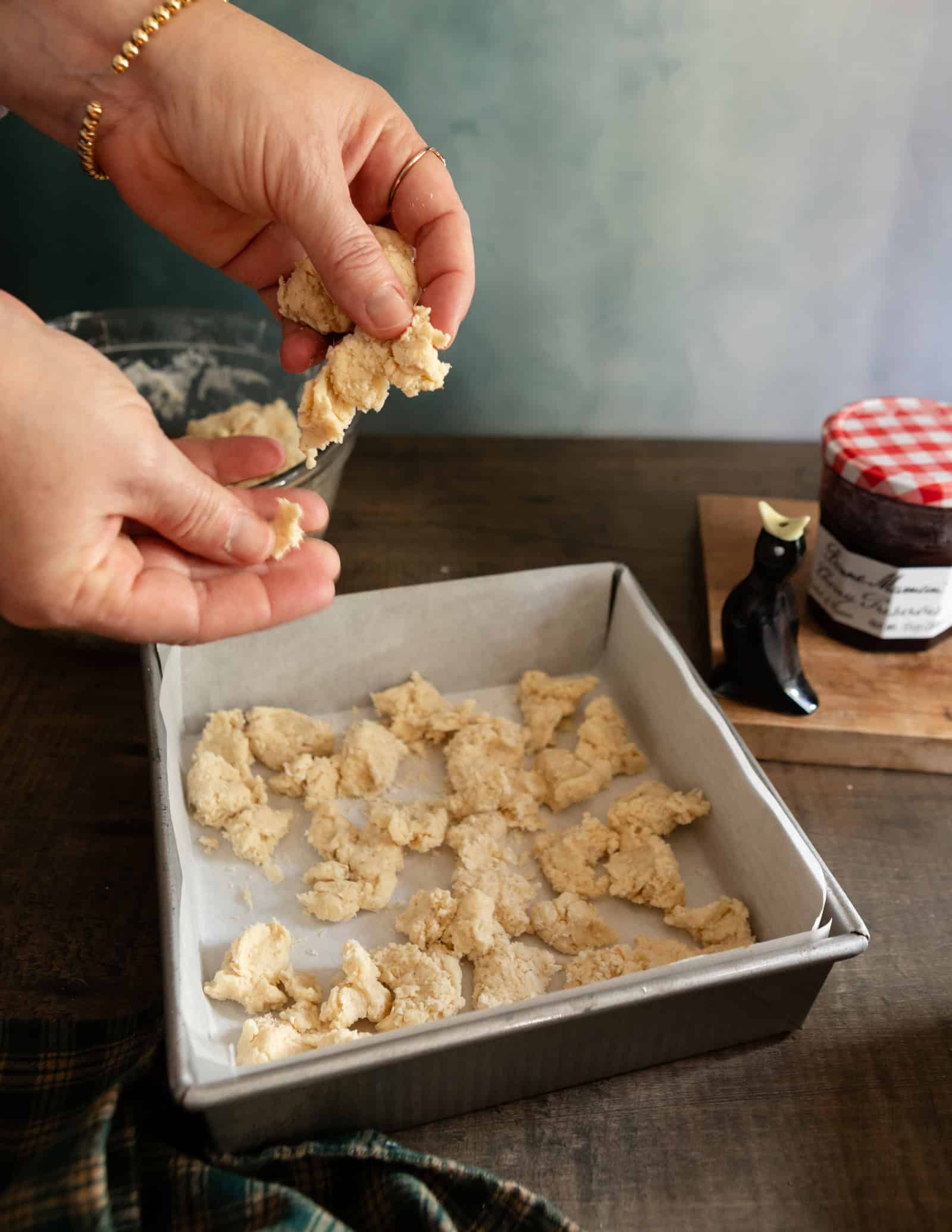 Hands tearing pieces of buttermilk scone dough and dropping them into a baking pan.