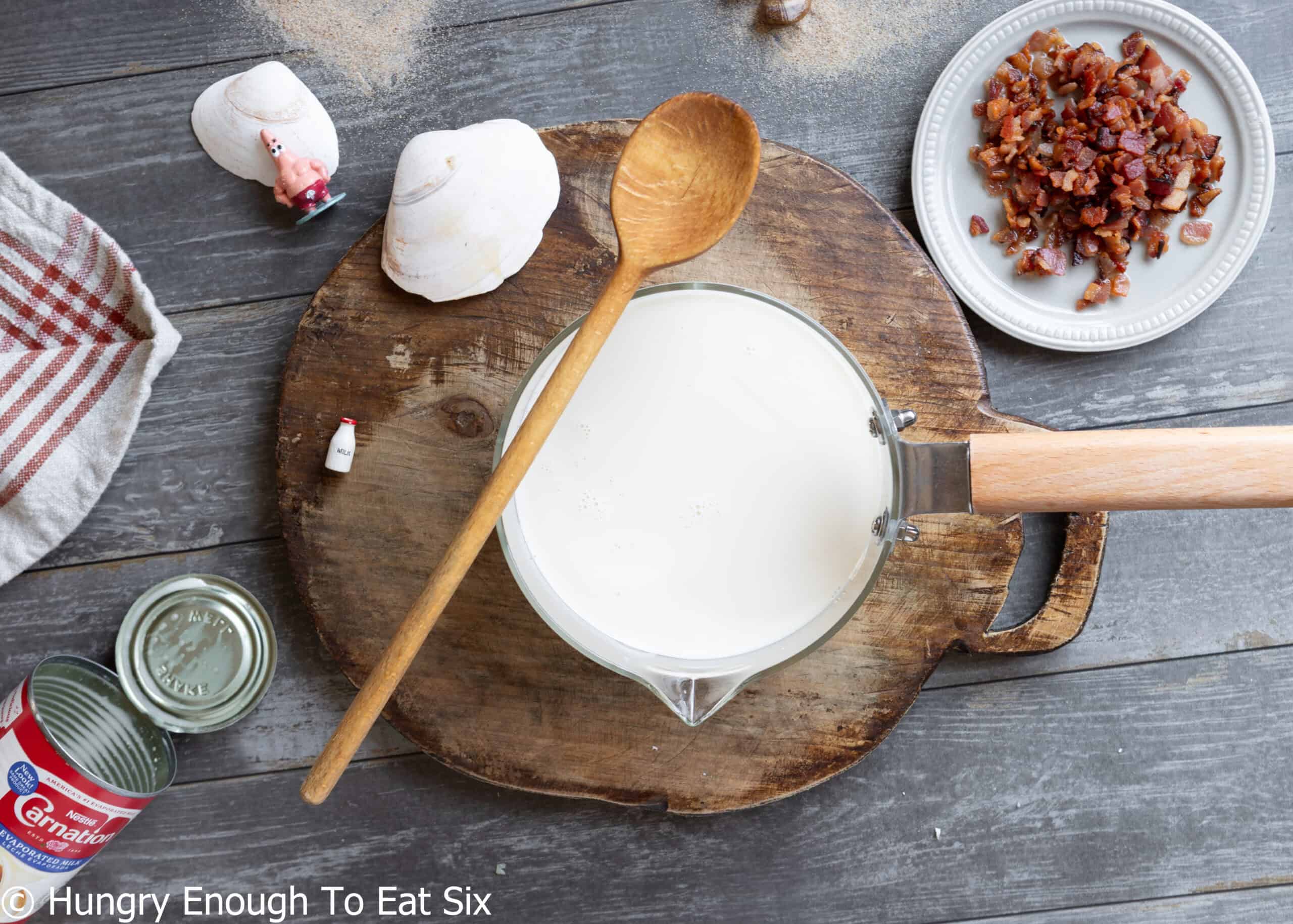 Small glass saucepan with milk and a wooden spoon, heating up for no-clam chowder.