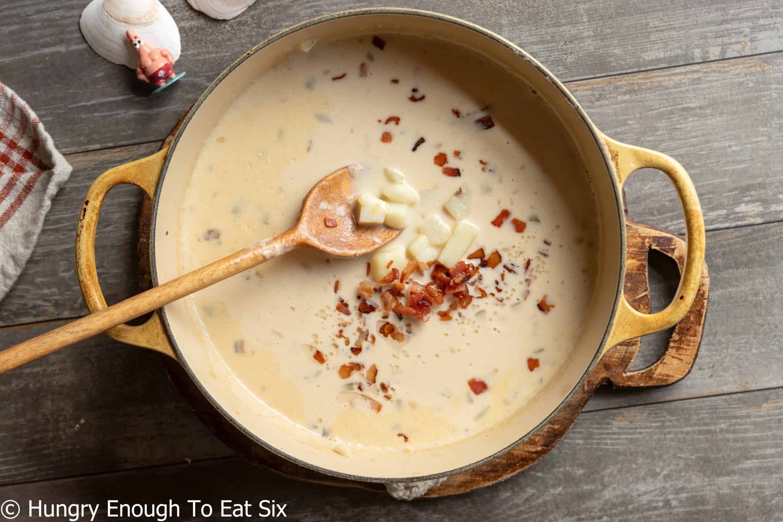 Dutch oven with a wooden spoon and a large quantity of New England no-clam chowder.