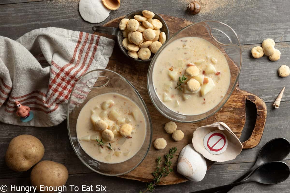 Two glass bowls of New England no-clam chowder with crackers and seashells.