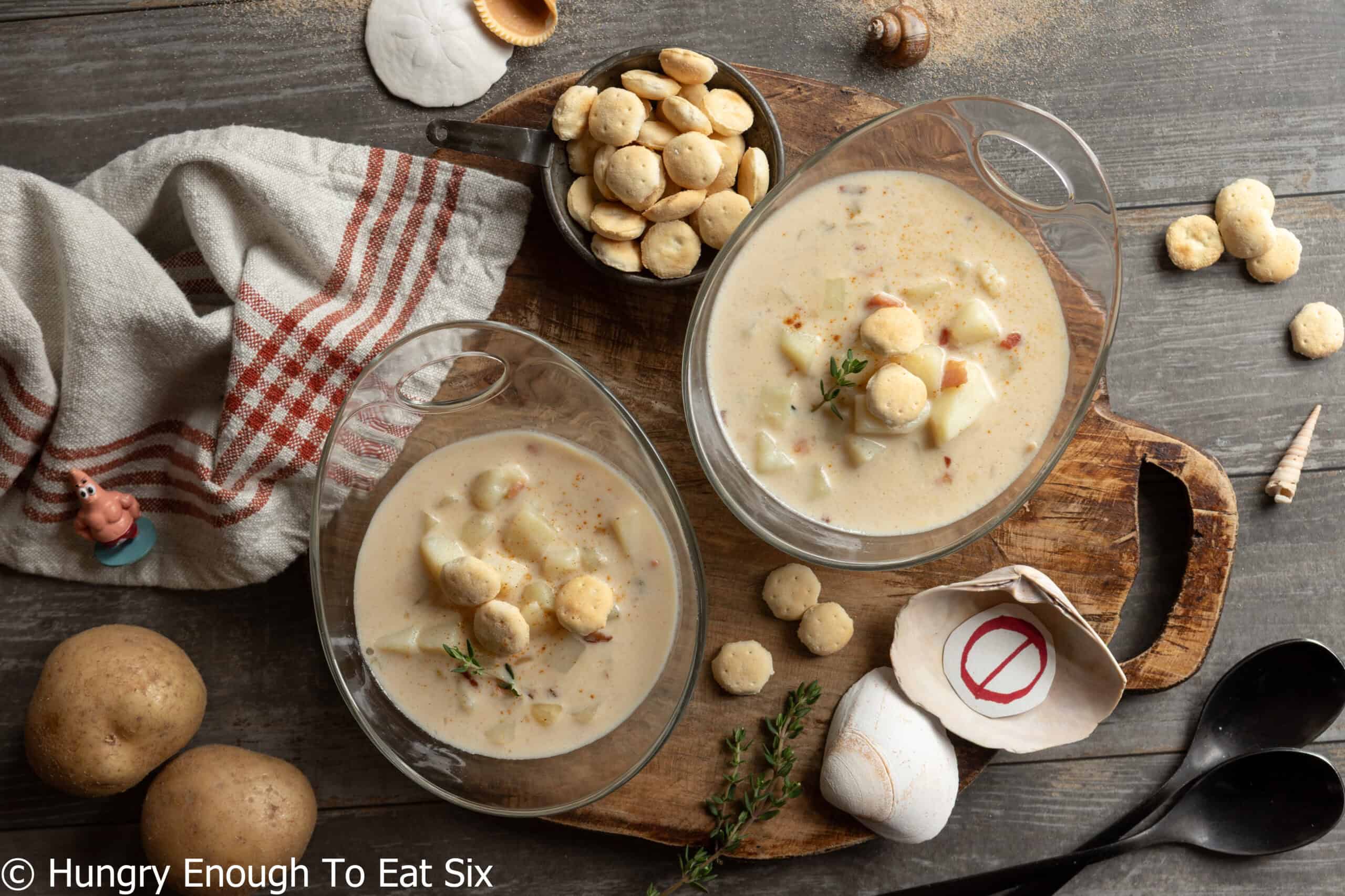 Two glass bowls of New England no-clam chowder with crackers and seashells.