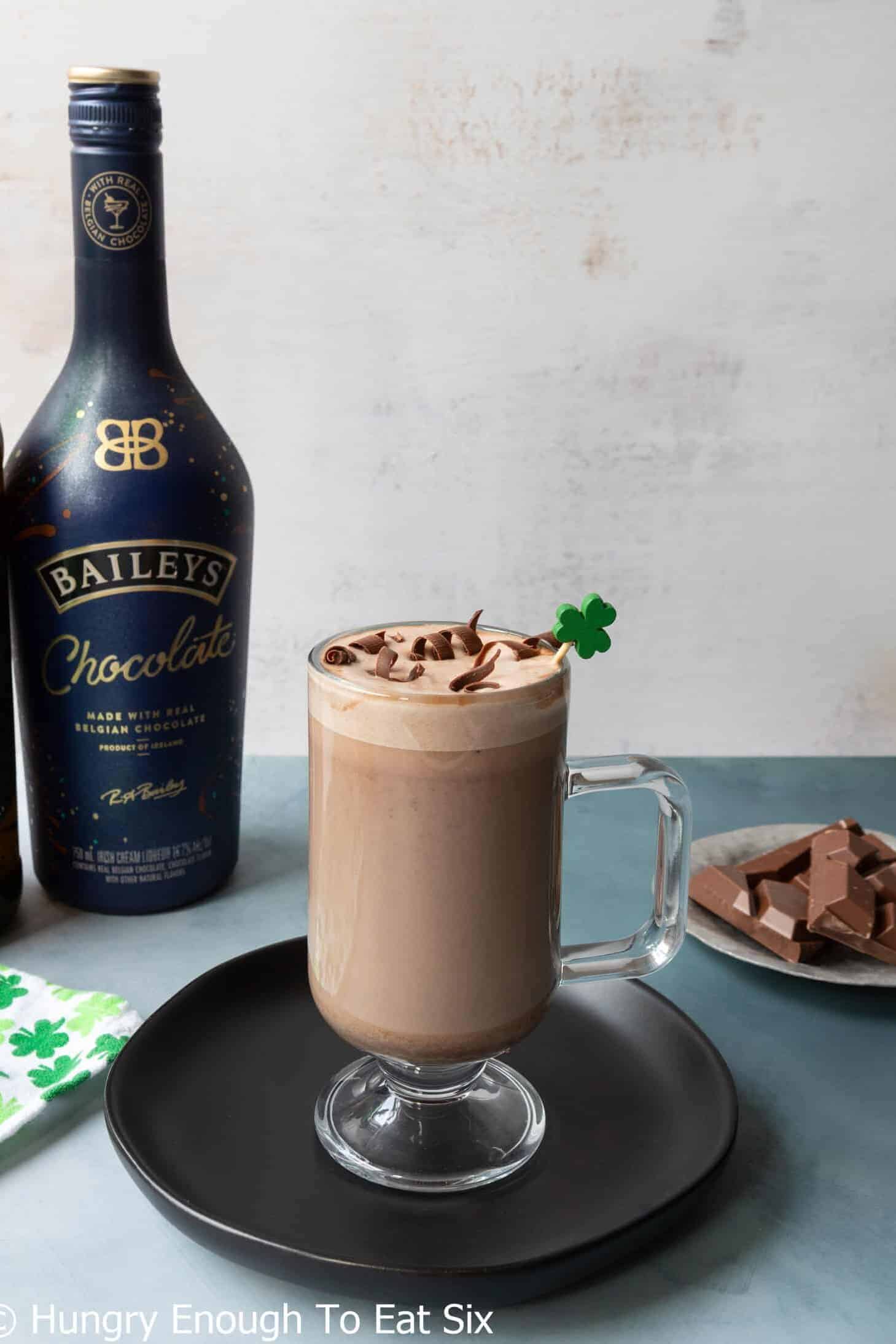 Irish coffee with liquor bottles and pieces of chocolate nearby.
