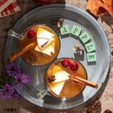 Gray plate with cups of hot apple cider with spices.