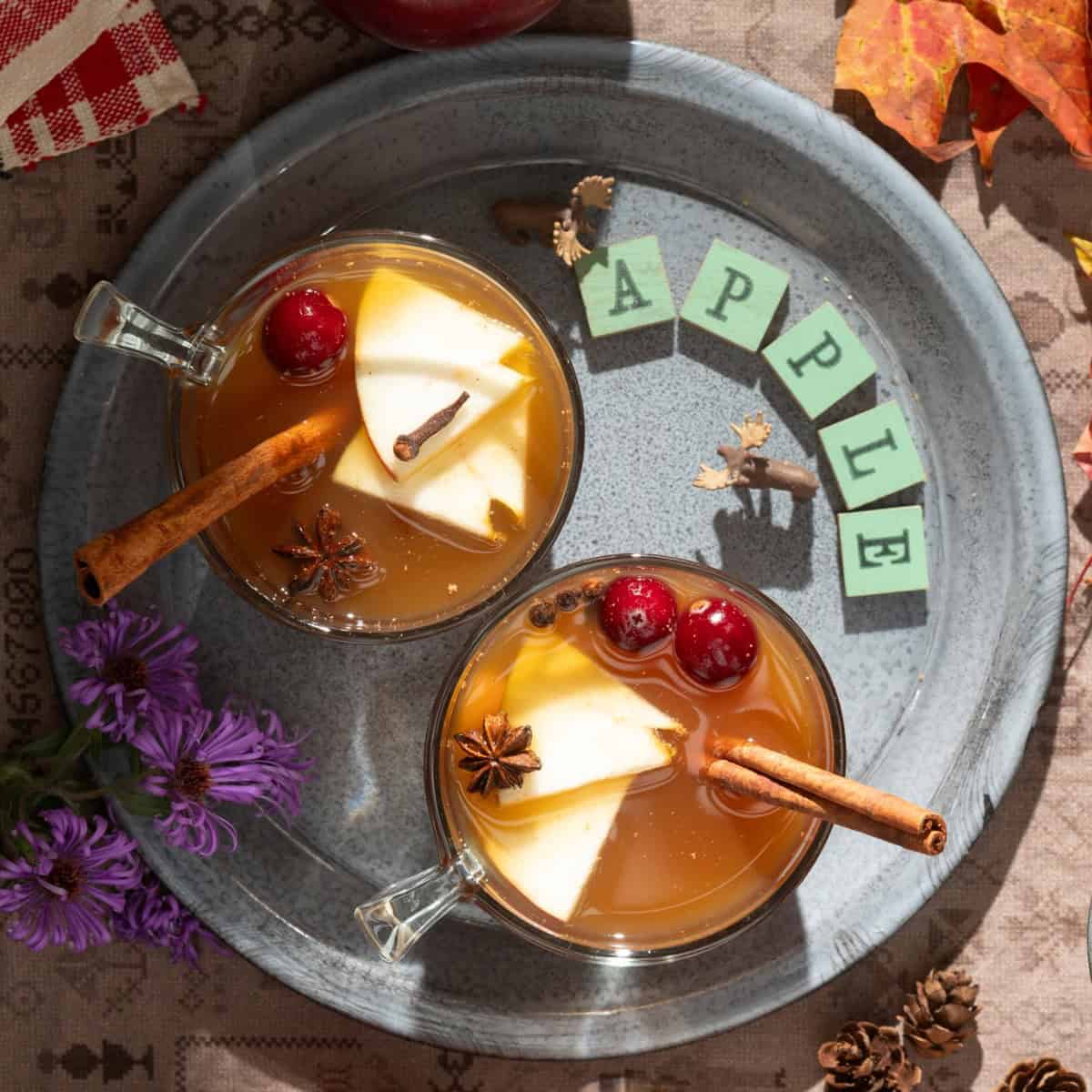 Gray plate with cups of hot apple cider with spices.