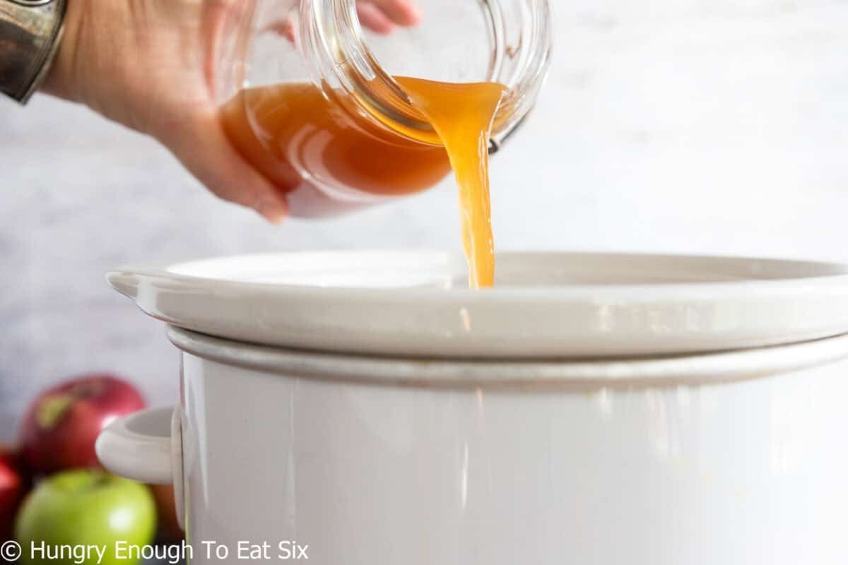 Apple cider pouring into a crock pot.